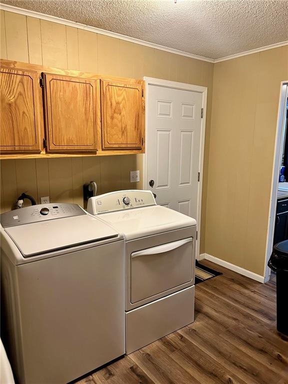 clothes washing area featuring cabinets, dark hardwood / wood-style flooring, a textured ceiling, washer and clothes dryer, and ornamental molding