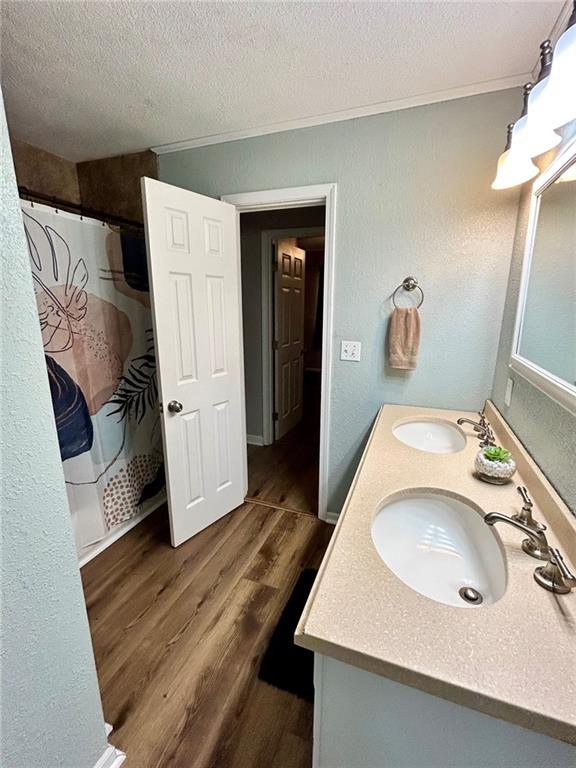 bathroom featuring walk in shower, hardwood / wood-style floors, a textured ceiling, vanity, and ornamental molding