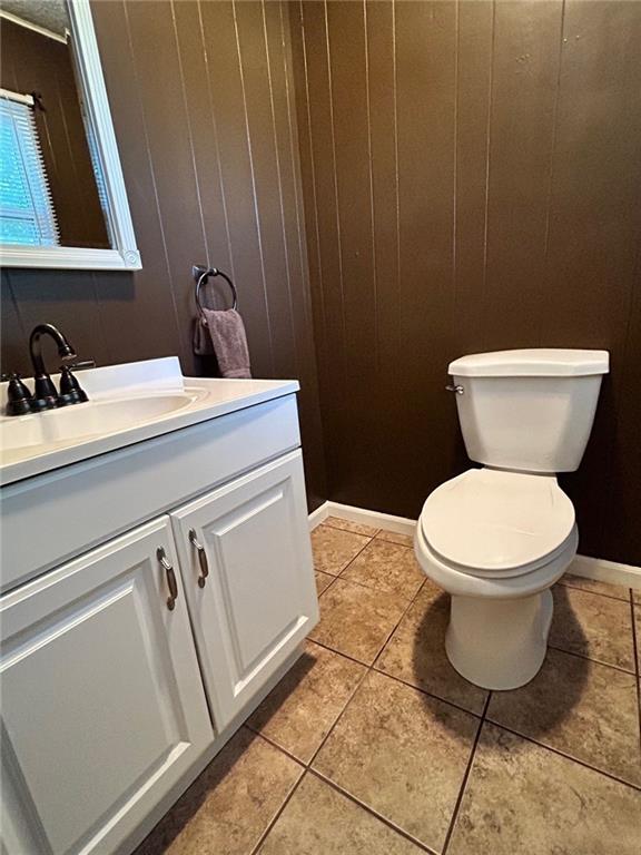 bathroom featuring tile patterned flooring, vanity, toilet, and wooden walls