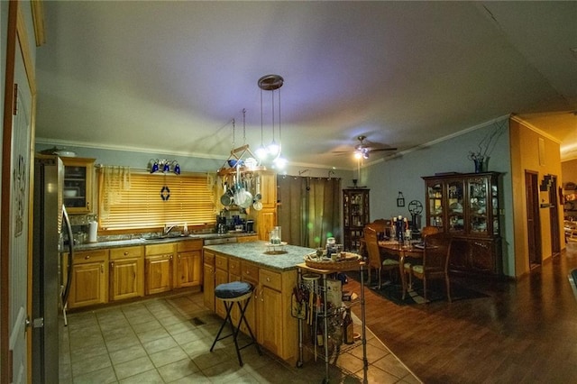 kitchen featuring ceiling fan, light wood-type flooring, a center island, ornamental molding, and stainless steel refrigerator