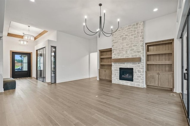 8736 N Lewis Ave, Kansas City, MO 64157 - unfurnished living room featuring a chandelier, light wood-style floors, a stone fireplace, and baseboards
