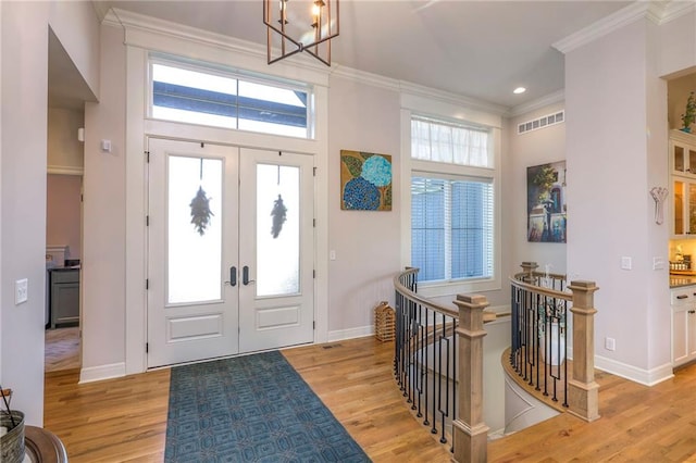 foyer featuring ornamental molding, a notable chandelier, light hardwood / wood-style flooring, and french doors