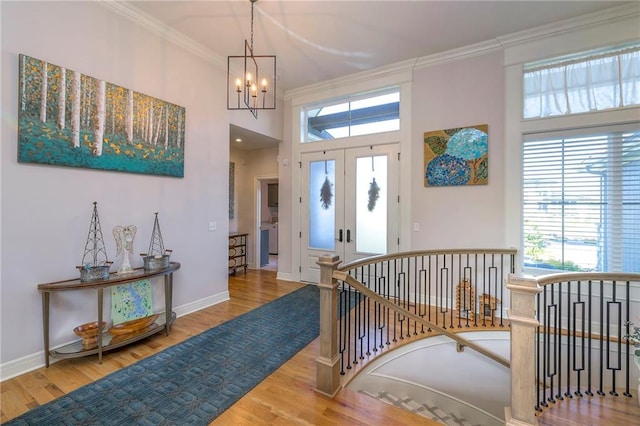 foyer with wood-type flooring, french doors, a chandelier, and ornamental molding