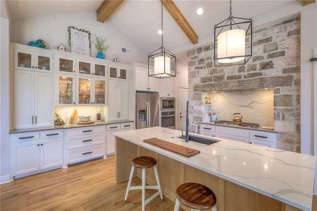 kitchen with decorative light fixtures, beamed ceiling, light stone counters, light hardwood / wood-style floors, and appliances with stainless steel finishes