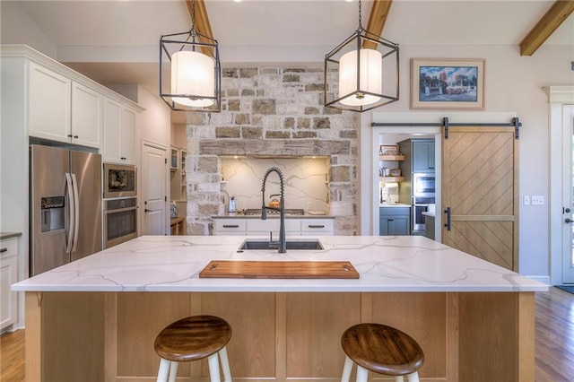 kitchen featuring light hardwood / wood-style floors, appliances with stainless steel finishes, a barn door, and beam ceiling