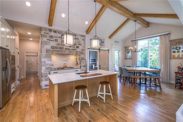 kitchen featuring pendant lighting, an island with sink, beamed ceiling, light stone counters, and light hardwood / wood-style floors