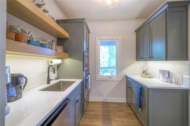 kitchen with tasteful backsplash, gray cabinets, hardwood / wood-style floors, appliances with stainless steel finishes, and sink