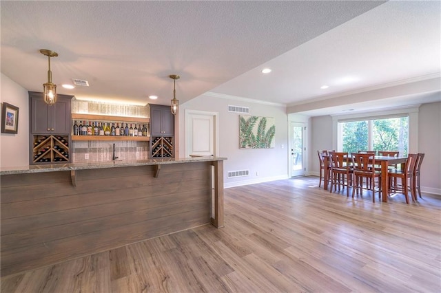 bar with light hardwood / wood-style flooring, light stone counters, hanging light fixtures, backsplash, and ornamental molding