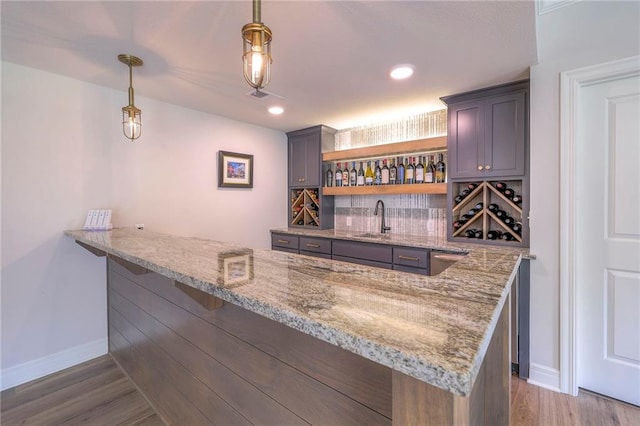 bar featuring pendant lighting, sink, light stone countertops, light hardwood / wood-style flooring, and backsplash