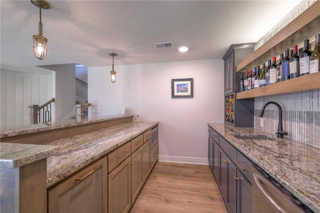 bar with sink, light hardwood / wood-style floors, decorative light fixtures, light stone countertops, and dishwasher