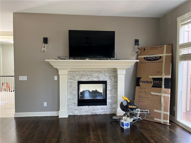 living room with a stone fireplace and dark wood-type flooring