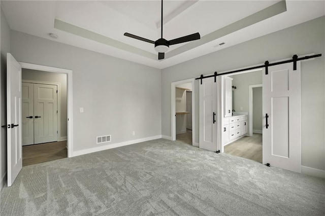 unfurnished bedroom featuring a walk in closet, light colored carpet, a raised ceiling, and a barn door