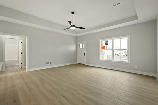 interior space featuring ceiling fan, a tray ceiling, and light wood-type flooring