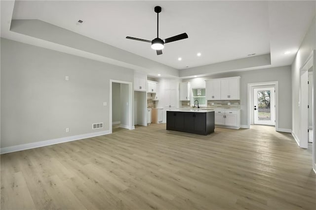 kitchen featuring baseboards, visible vents, light wood finished floors, white cabinets, and a raised ceiling