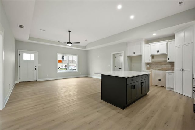 kitchen with a raised ceiling, white cabinets, light wood-style flooring, and visible vents