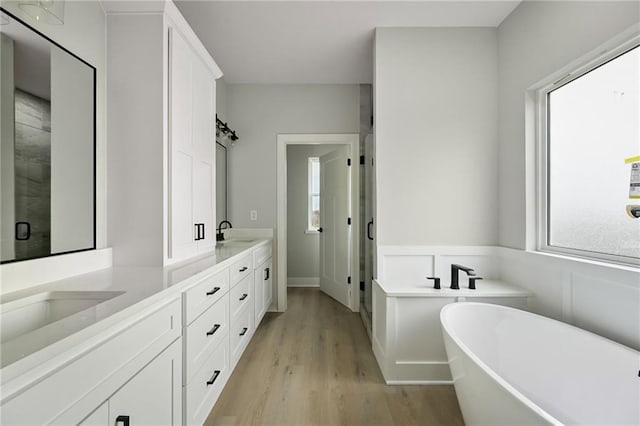 bathroom with a sink, wood finished floors, a shower stall, double vanity, and a freestanding bath