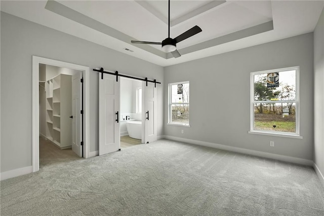 unfurnished bedroom featuring a walk in closet, baseboards, a barn door, a tray ceiling, and carpet floors