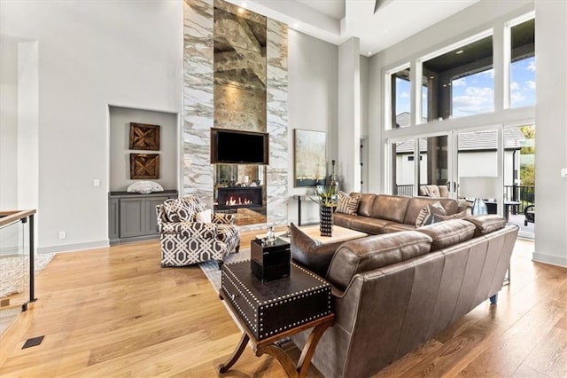 6101 NW 58th St, Kansas City, MO 64151 - living room with a high ceiling, light wood-style flooring, a tiled fireplace, and baseboards