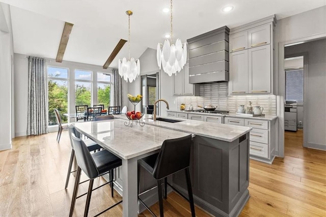 6101 NW 58th St, Kansas City, MO 64151 - kitchen with a sink, a chandelier, gray cabinetry, stainless steel gas cooktop, and custom exhaust hood