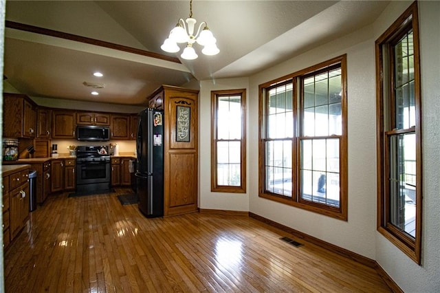 kitchen with hardwood / wood-style flooring, black appliances, lofted ceiling, decorative light fixtures, and a chandelier