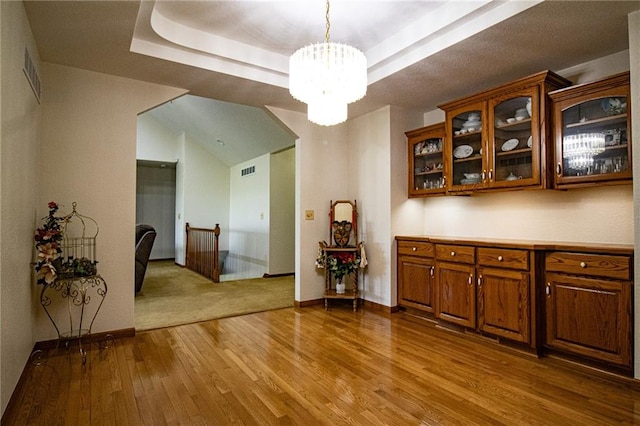 interior space with a raised ceiling, an inviting chandelier, and light hardwood / wood-style flooring