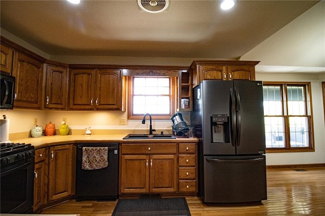 kitchen featuring light hardwood / wood-style flooring, black appliances, vaulted ceiling, and sink