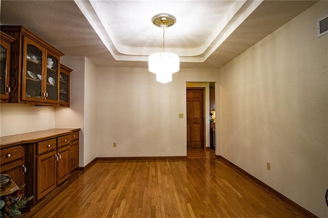 unfurnished dining area featuring wood-type flooring, an inviting chandelier, and a raised ceiling