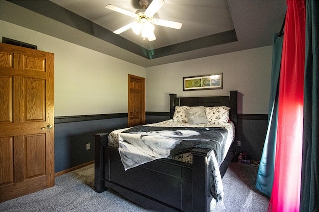 carpeted bedroom with a raised ceiling and ceiling fan