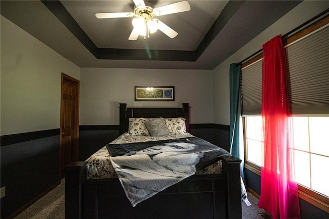 bedroom with a raised ceiling, ceiling fan, and dark carpet