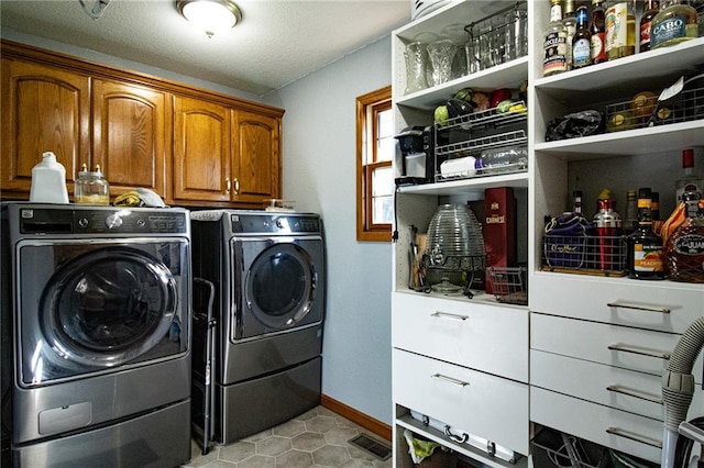 laundry area featuring cabinets, a textured ceiling, washing machine and clothes dryer, and light tile patterned floors