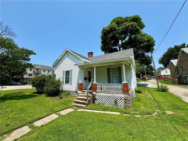 bungalow-style house featuring a shingled roof, a front lawn, covered porch, a chimney, and driveway