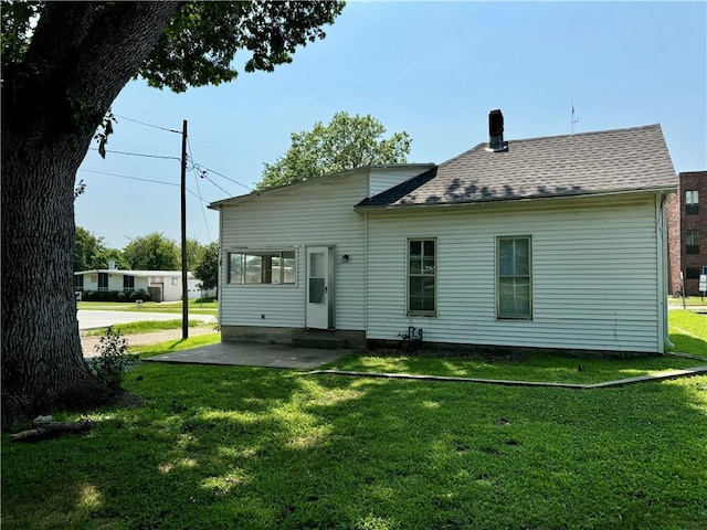 back of property with a lawn, entry steps, a patio, a shingled roof, and a chimney