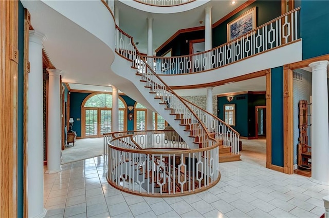 stairway with crown molding, a towering ceiling, decorative columns, and tile patterned flooring