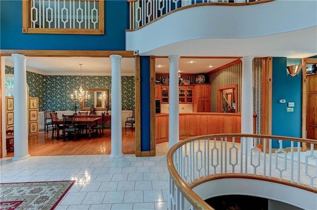 interior space featuring a towering ceiling, decorative columns, ornamental molding, and a chandelier