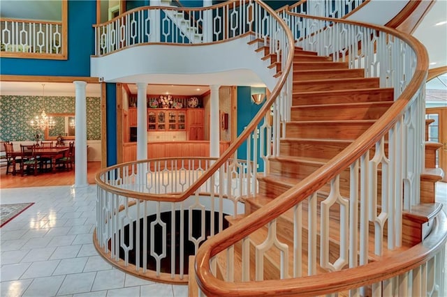 stairway with tile patterned flooring, an inviting chandelier, a towering ceiling, and decorative columns