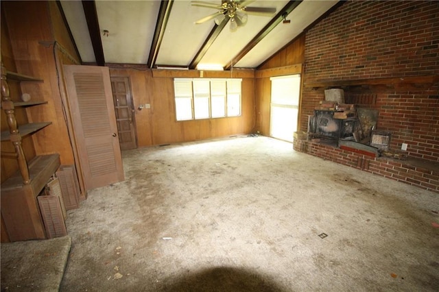 unfurnished living room featuring vaulted ceiling with beams, light carpet, a wood stove, wooden walls, and ceiling fan