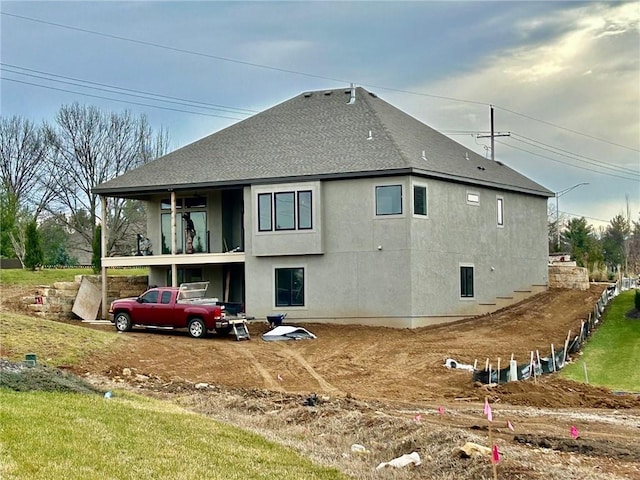 rear view of property featuring a shingled roof, a balcony, and stucco siding