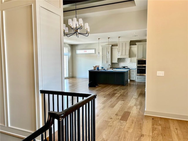 kitchen with pendant lighting, stainless steel appliances, light countertops, light wood-style floors, and a kitchen island with sink