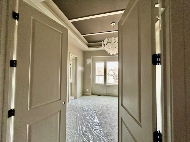 hall featuring a chandelier, carpet, a raised ceiling, and baseboards