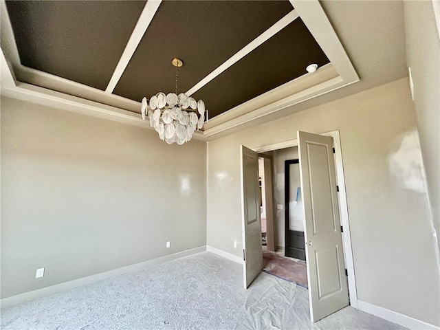 carpeted empty room featuring baseboards, a raised ceiling, and a notable chandelier