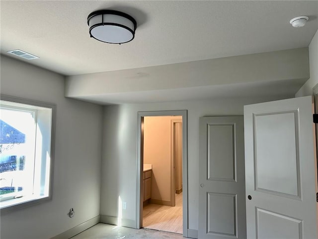 unfurnished bedroom with light wood-style floors, ensuite bath, visible vents, and baseboards