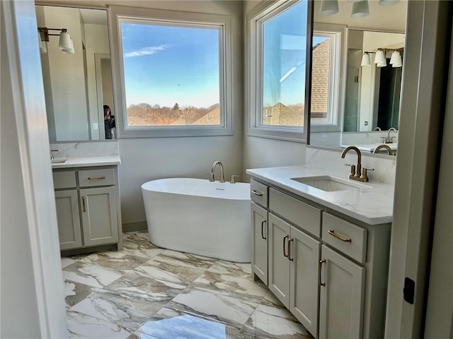 full bathroom featuring a freestanding tub, marble finish floor, two vanities, and a sink