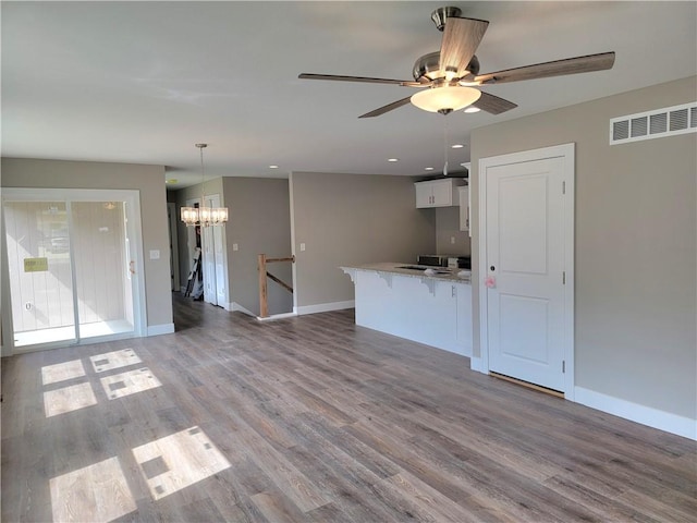 kitchen with light stone countertops, ceiling fan with notable chandelier, hanging light fixtures, white cabinetry, and hardwood / wood-style flooring