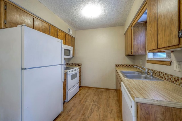 kitchen with sink, a textured ceiling, white appliances, and light hardwood / wood-style flooring