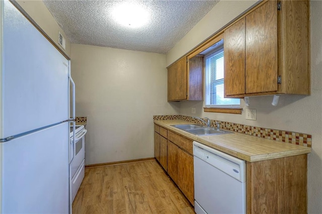 kitchen featuring sink, white appliances, light hardwood / wood-style floors, and a textured ceiling