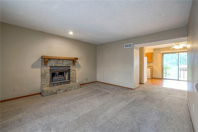 unfurnished living room featuring ceiling fan, a stone fireplace, light carpet, and a textured ceiling