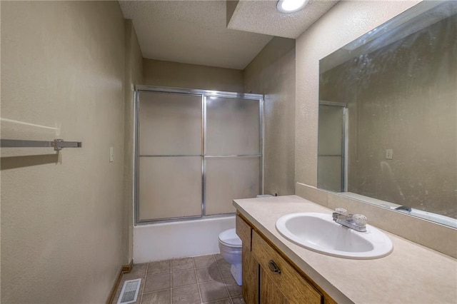 full bathroom with shower / bath combination with glass door, vanity, a textured ceiling, tile patterned floors, and toilet