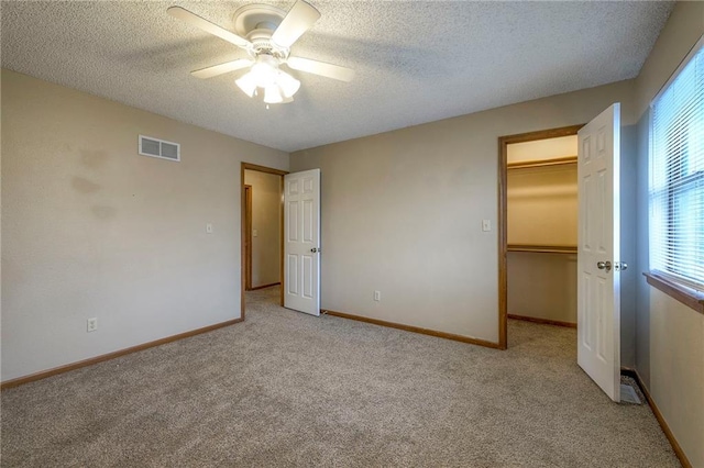 unfurnished bedroom with ceiling fan, a spacious closet, light carpet, and a textured ceiling