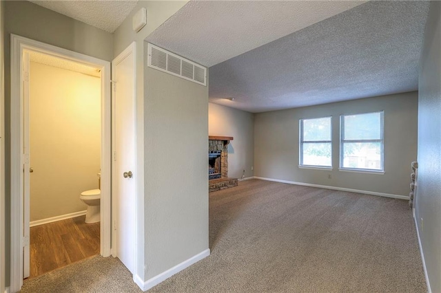 unfurnished living room with a stone fireplace, carpet floors, and a textured ceiling