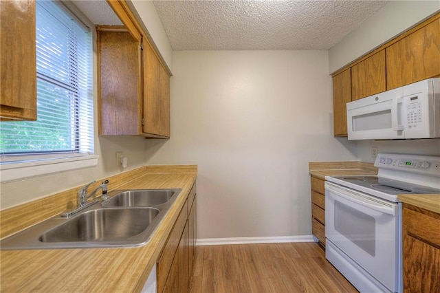 kitchen with sink, a textured ceiling, white appliances, and light hardwood / wood-style flooring